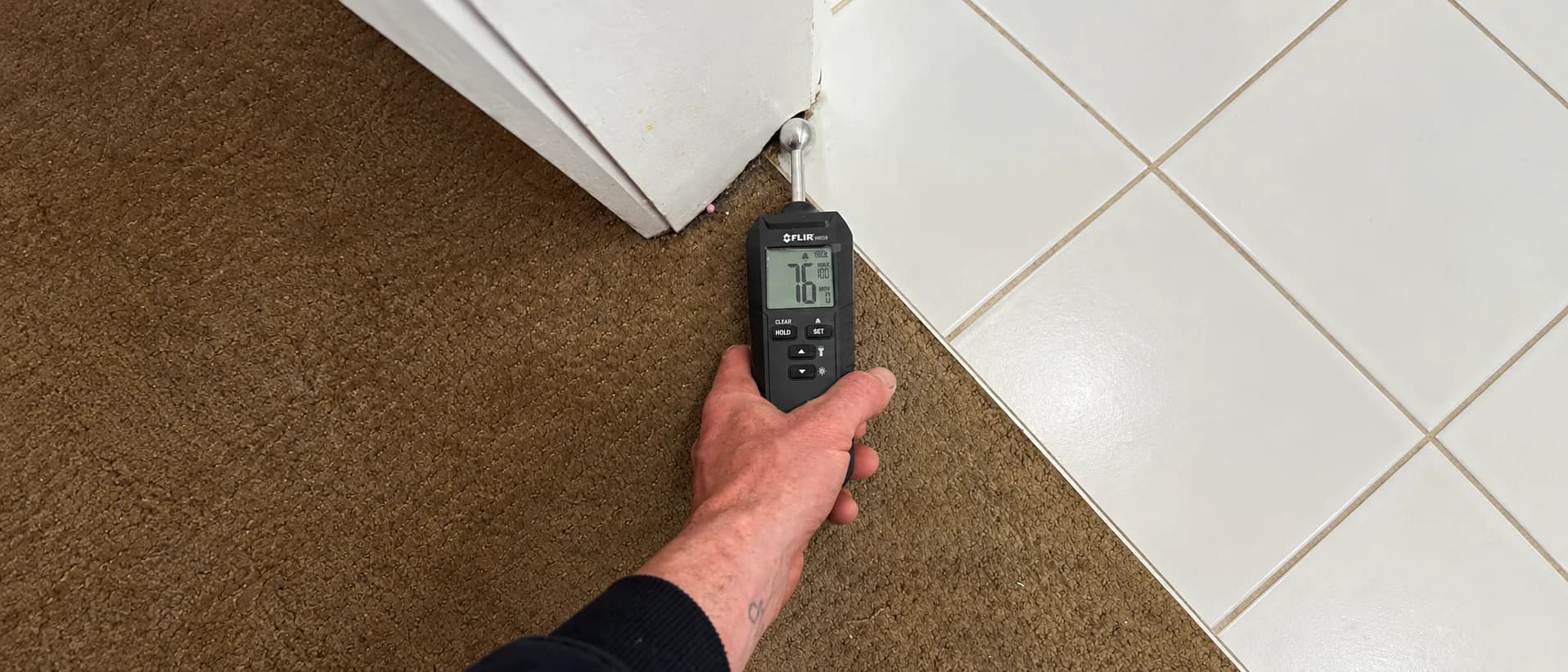 FLIR moisture meter testing the carpet and tile seam during a leak investigation