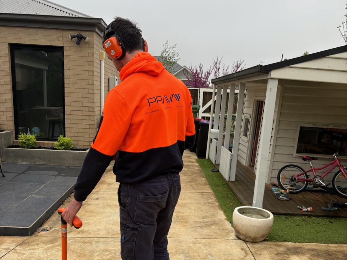 Prava technician using acoustic leak detection equipment on a residential driveway